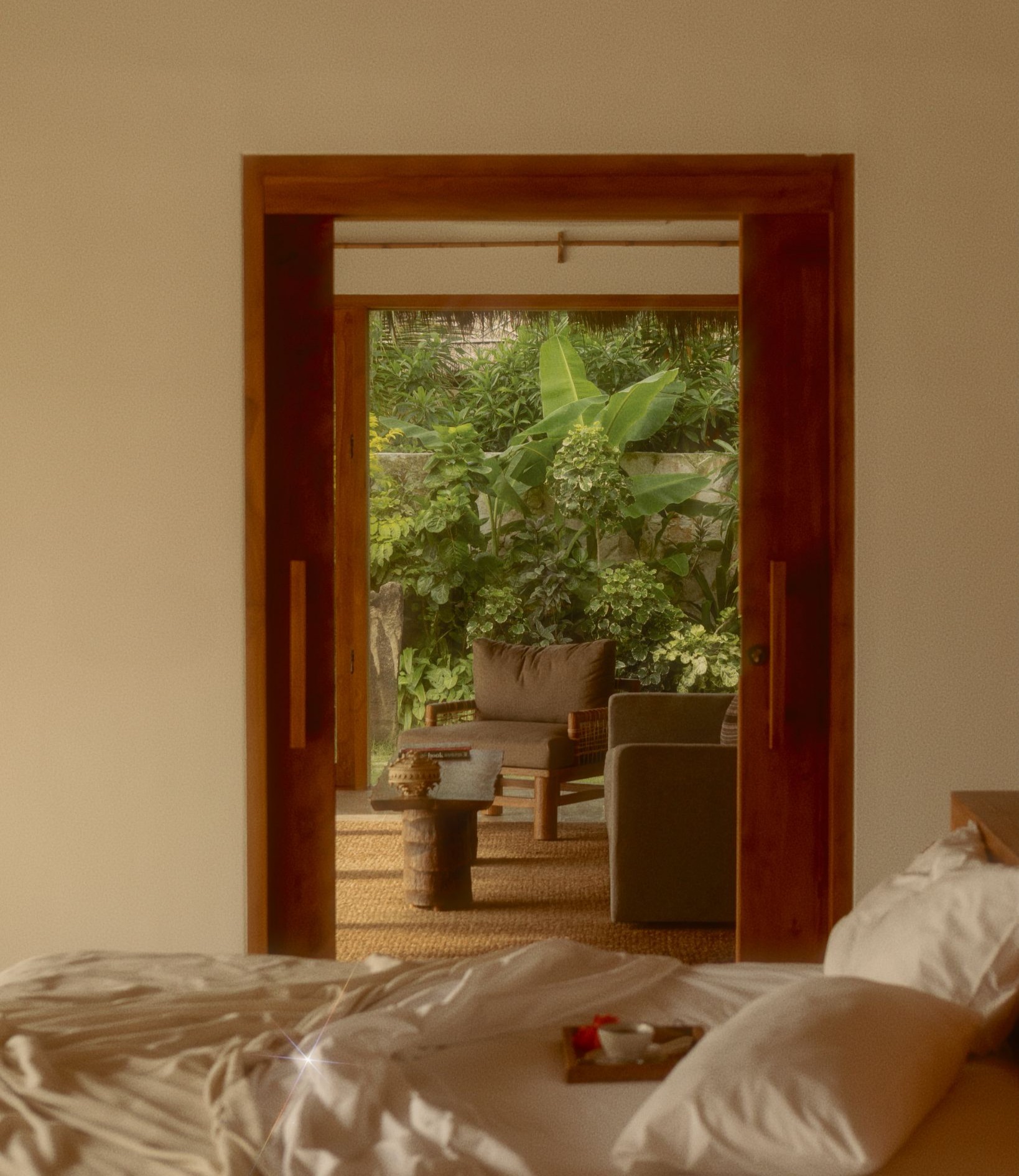 Cozy bedroom interior of a villa at The Sanubari looking out through open sliding doors onto a lush tropical garden seating area.