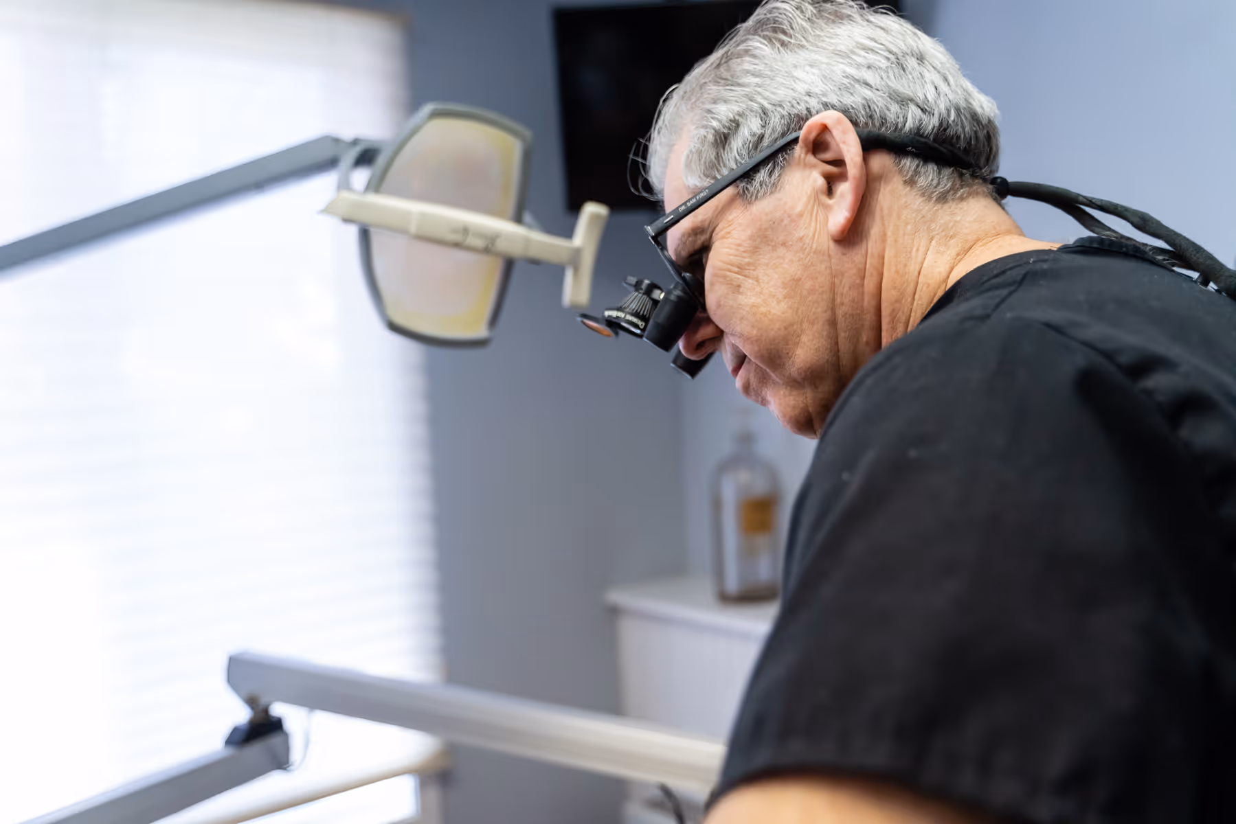 A man in a dentist's chair looking through a magnifying glass.