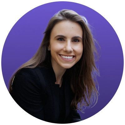 Smiling woman with long brown hair wearing a black jacket against a purple background.