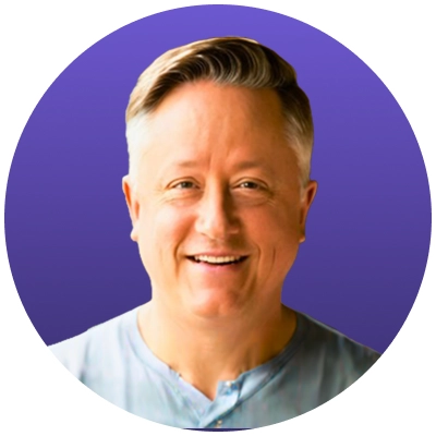 Smiling middle-aged man with light skin and short grayish-blond hair against a purple background.