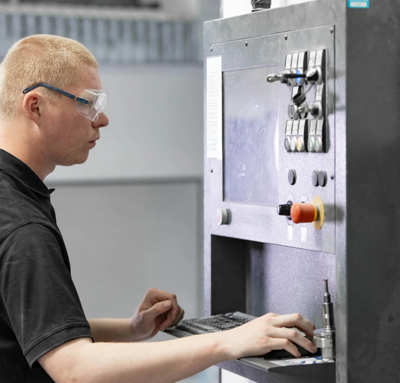 Machine operator in safety glasses at a CNC control panel at Shape