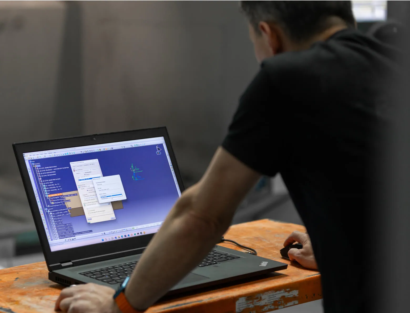Programmer working on CAM toolpaths on a laptop beside a machine at Shape