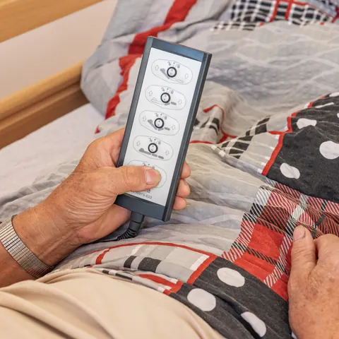 Senior drží ruční ovladač elektrické polohovací postele