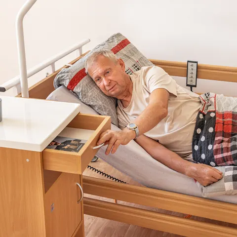 Senior na polohovací posteli si bere věc ze zásuvky nočního stolku
