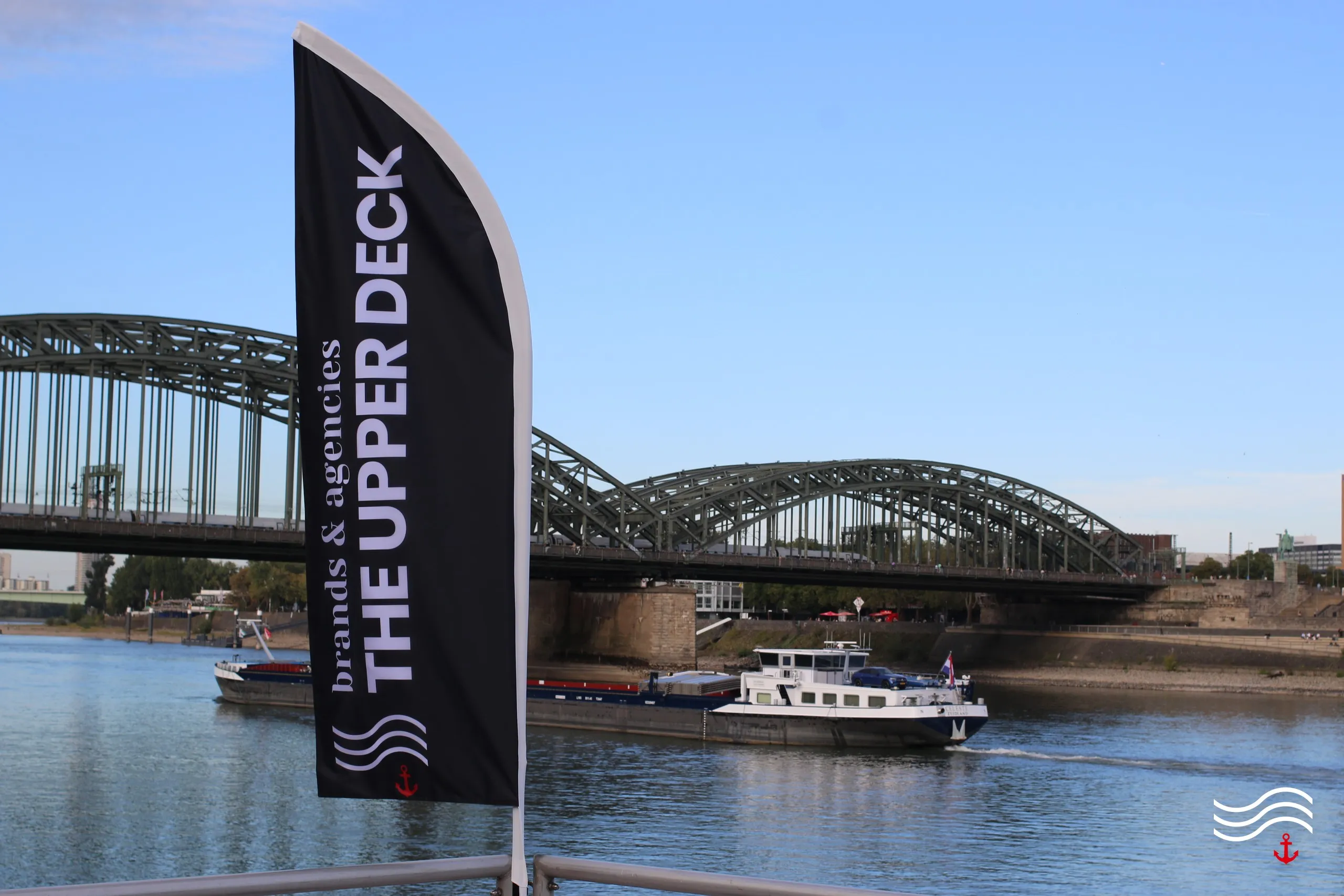 THE UPPER DECK Beachflag vor Rhein und Hohenzollernbrücke – brands & agencies THE UPPER DECK 2026 in Köln