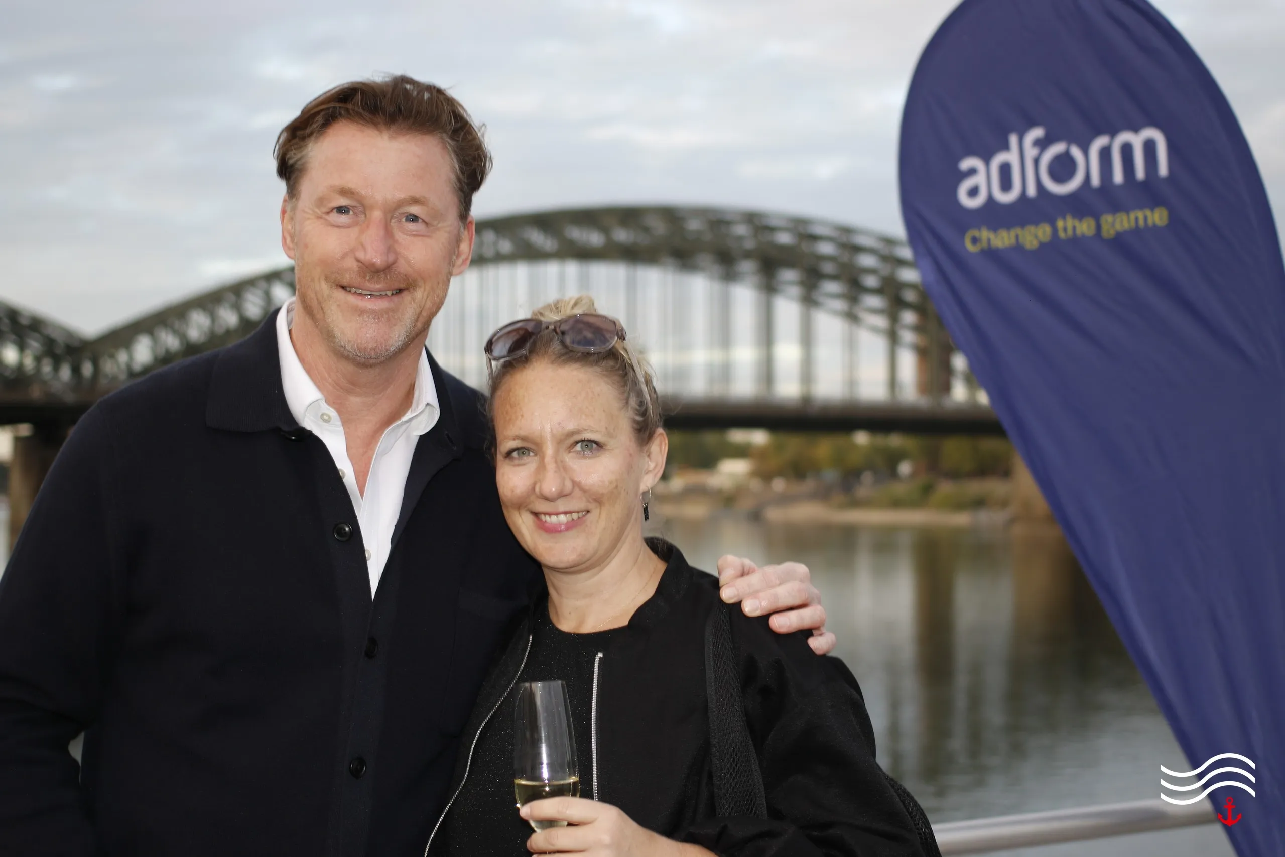 Zwei Gäste vor der Hohenzollernbrücke neben einer adform Beachflag – brands & agencies THE UPPER DECK 2026 in Köln