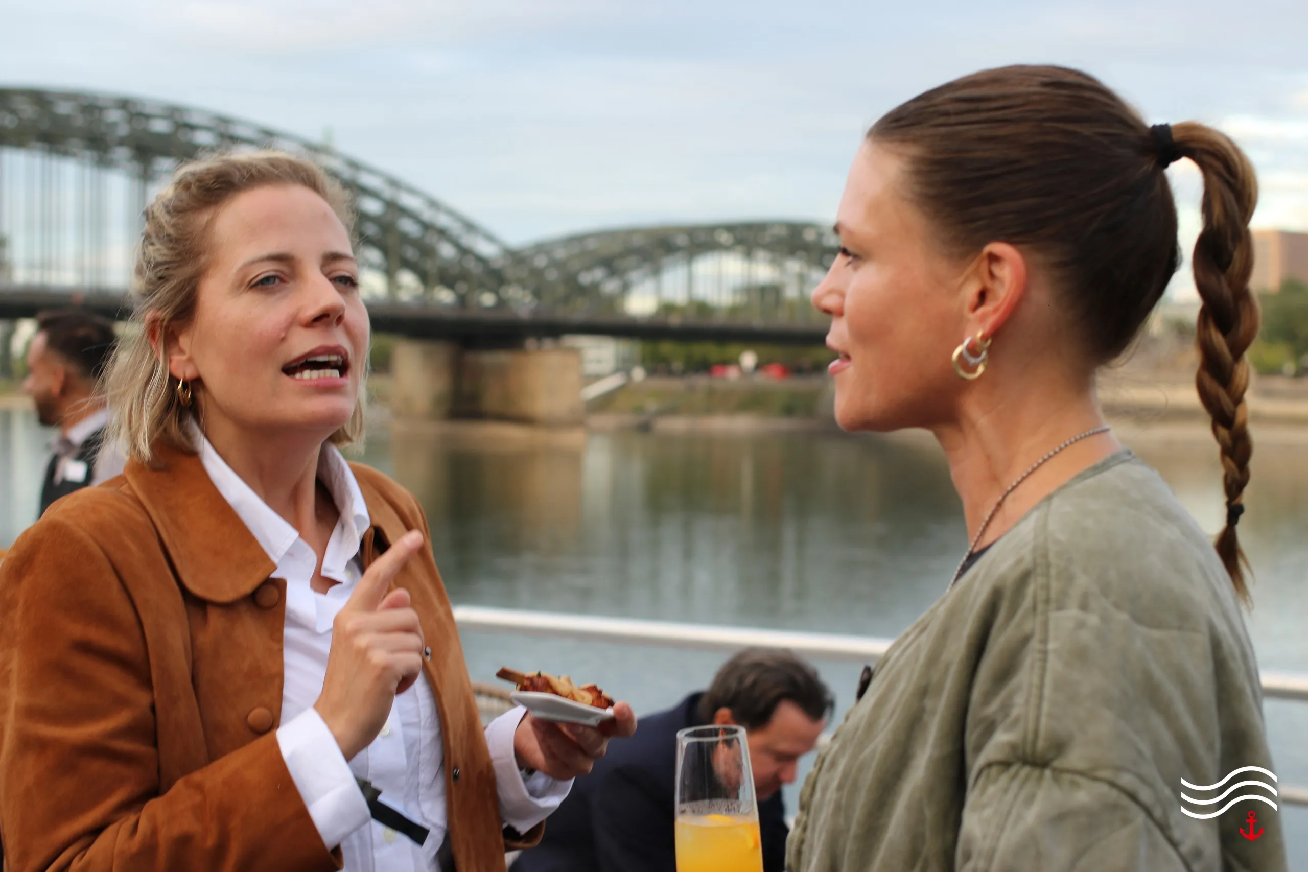 Zwei Gäste im Gespräch vor dem Rheinpanorama mit Hohenzollernbrücke – brands & agencies THE UPPER DECK 2026 in Köln