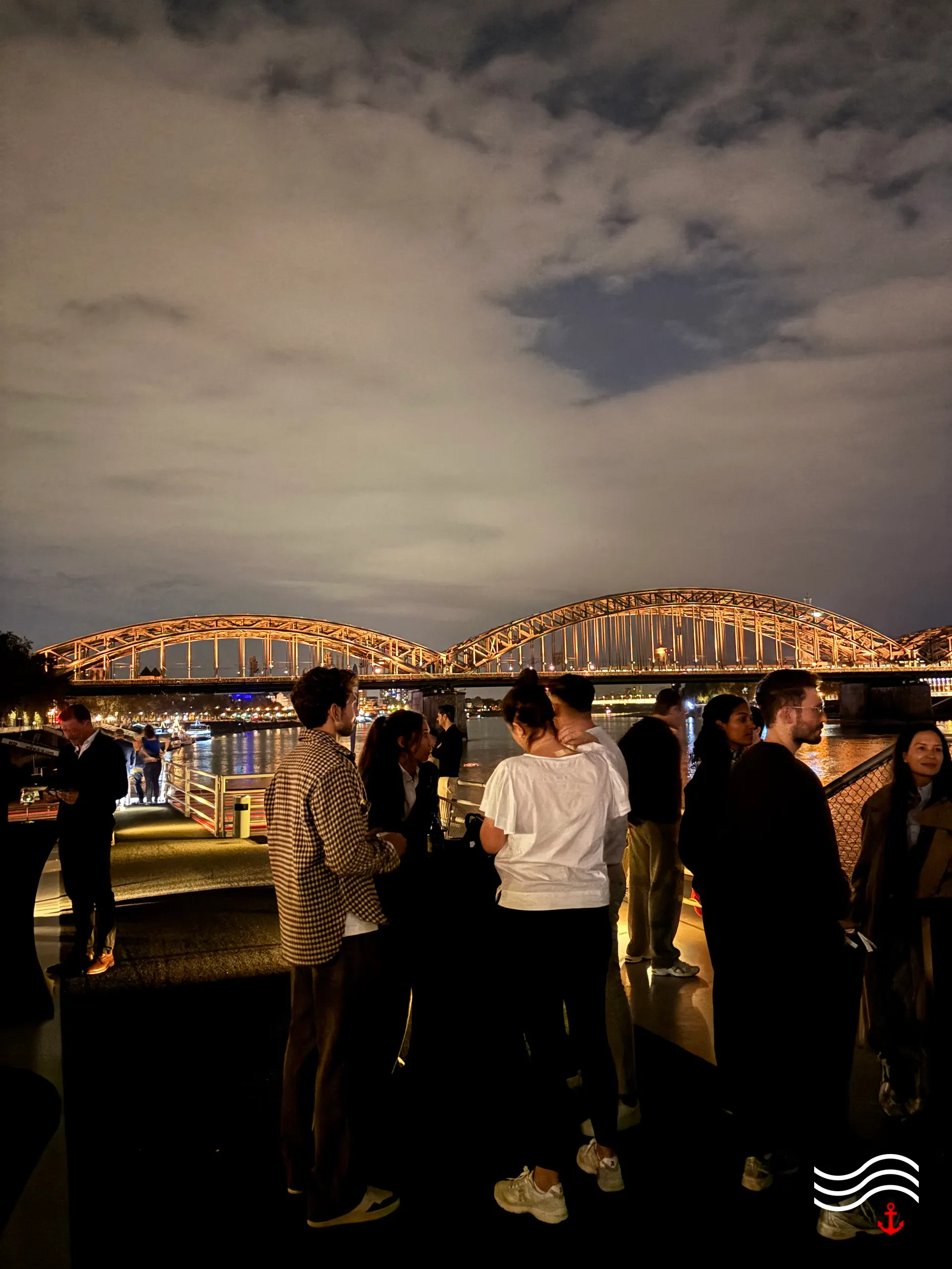 Gäste an Deck bei Nacht vor der beleuchteten Hohenzollernbrücke – brands & agencies THE UPPER DECK 2026 in Köln