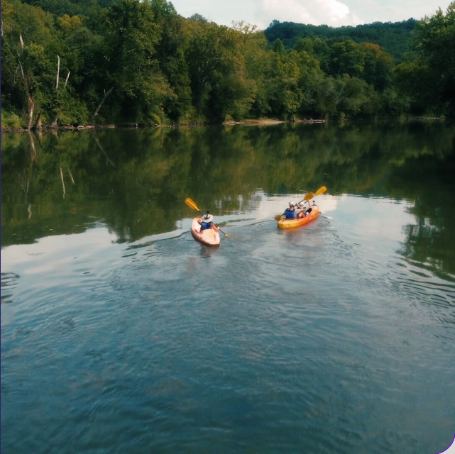 Two people kayaking in a river surrounded by trees