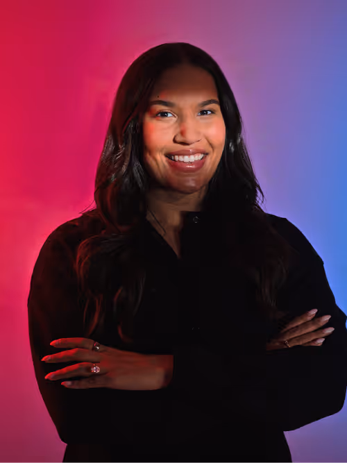 Smiling woman with long dark hair and crossed arms stands against a red and blue gradient background.
