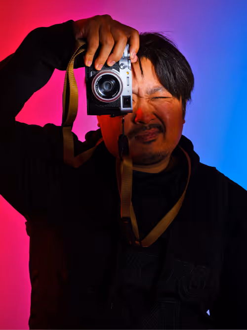 Man holding a camera up to his eye against a red and blue gradient background.