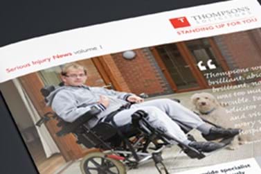 A man in a wheelchair sitting next to a dog in front of a red brick building.