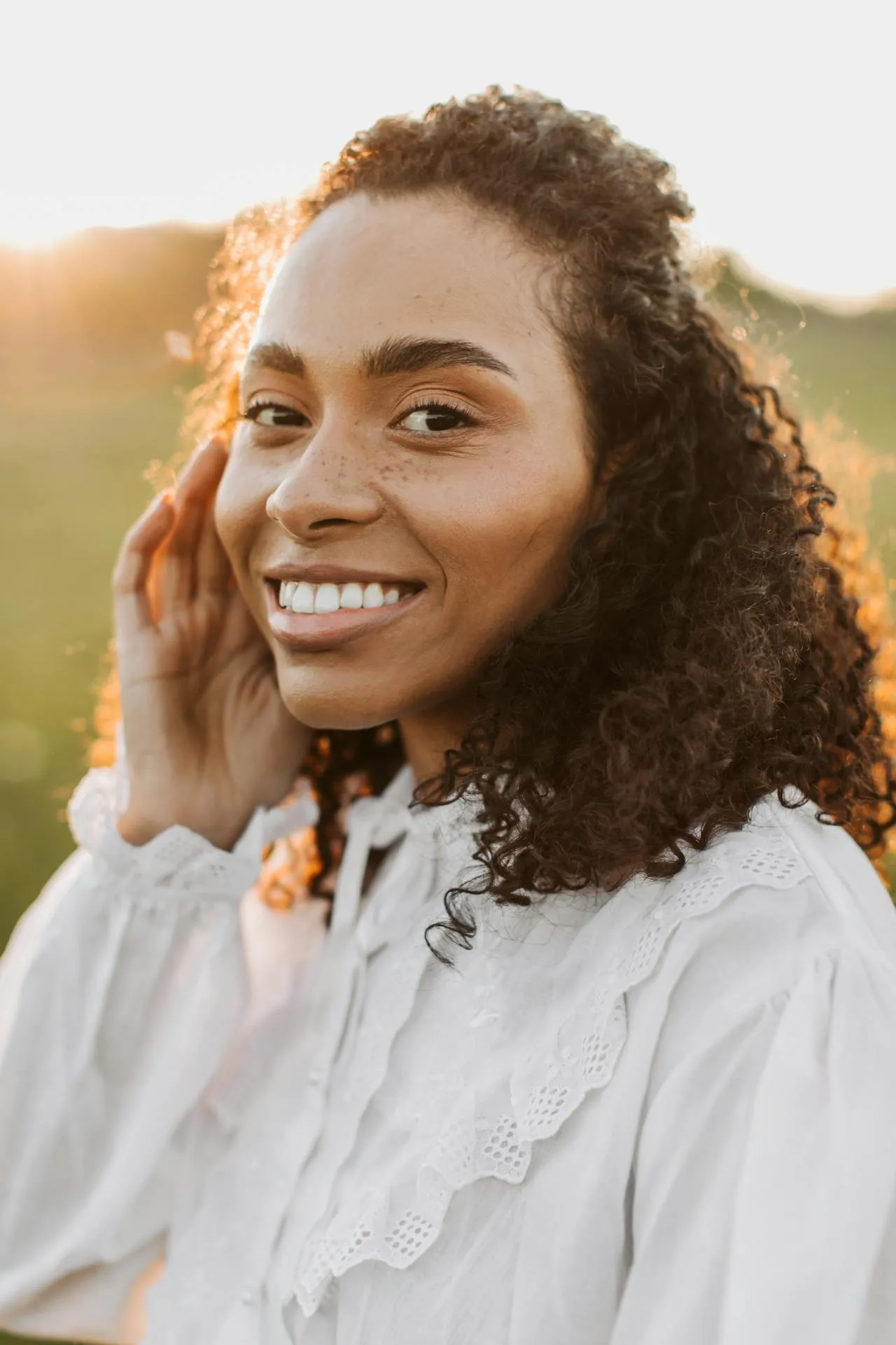 A woman with curly hair smiling and wearing a white blouse.