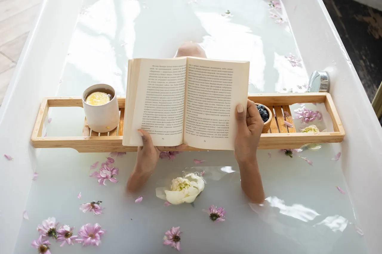 A person laying in a bathtub reading a book.