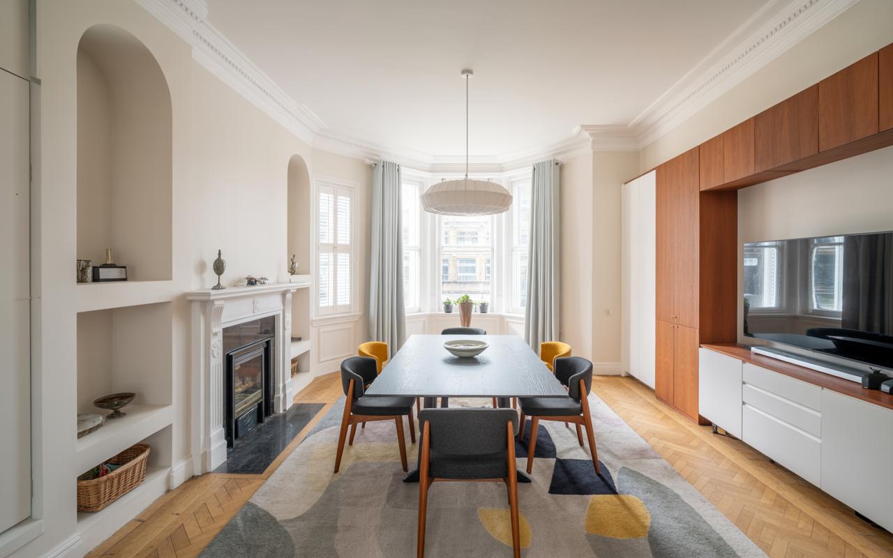A bright and elegant dining room blending modern design with classic architectural features. This interior showcases a stylish dining set, a traditional fireplace, and custom built-in wooden cabinetry, all set on a beautiful herringbone floor.