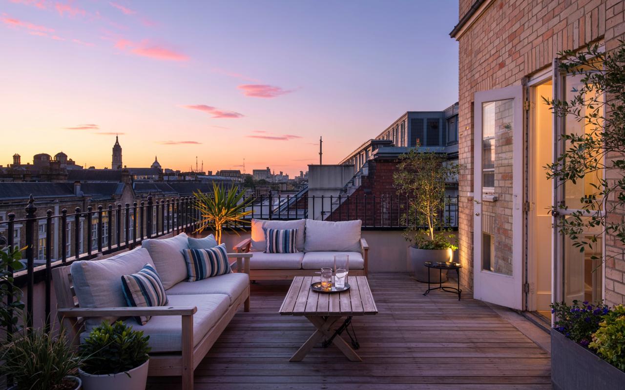 A luxurious rooftop terrace in London with comfortable outdoor sofas, offering a stunning view of the city skyline at sunset. This beautiful roof garden features elegant wooden decking and ambient lighting, creating the perfect urban retreat