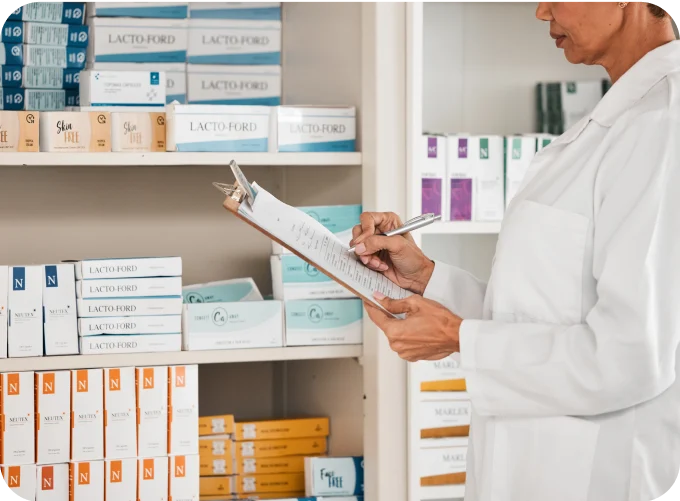Woman writing on a clipboard in front of pharmacy shelves stocked with medicine, representing the Pharmacy industry and Burq's delivery solutions for reliable and secure healthcare logistics.
