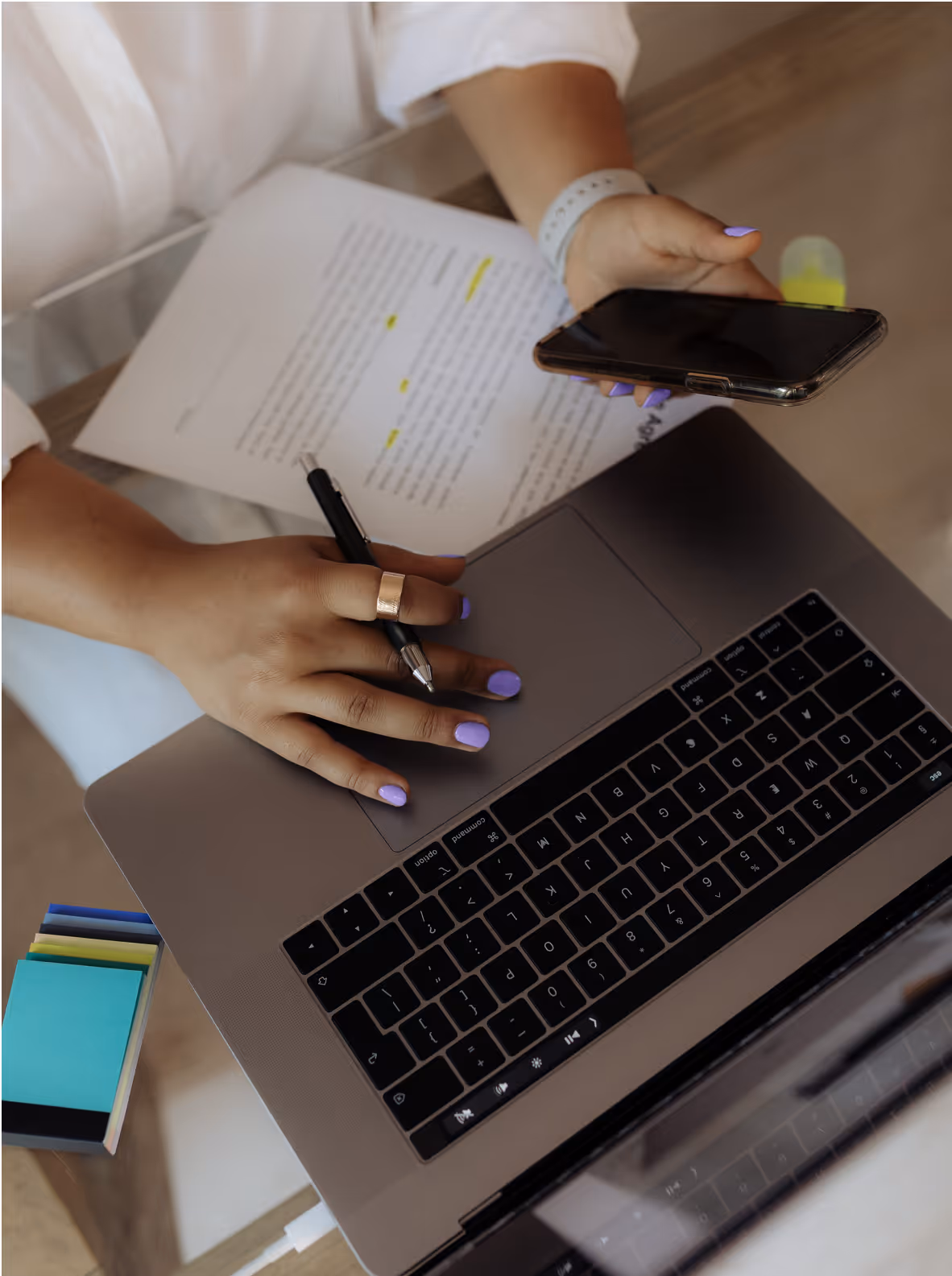 Hands typing on a laptop and looking at a phone with post-it notes on the side