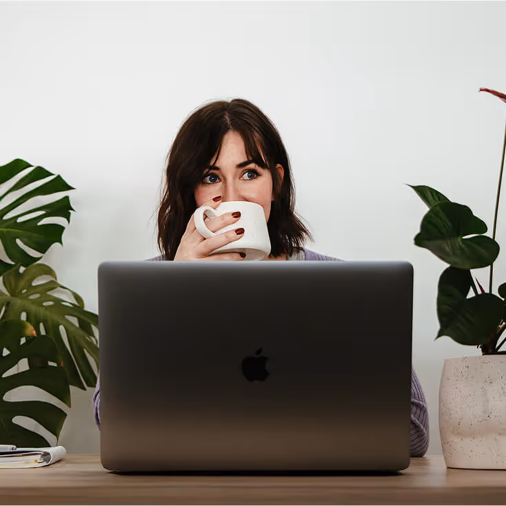 Laura sitting behind a laptop drinking coffee