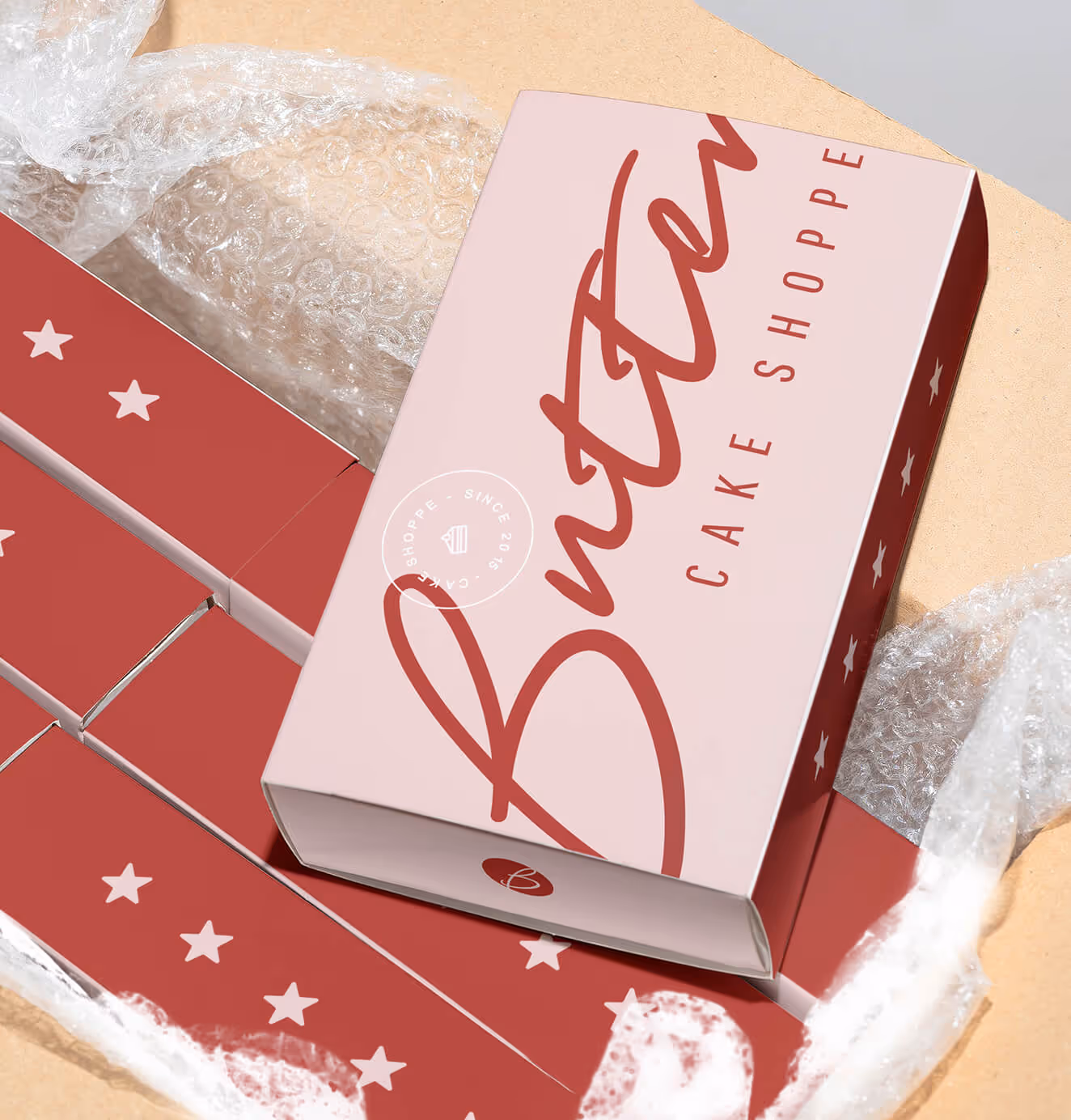 Pink Butter Cake Shoppe box with bold red script logo and star patterns, sitting inside a shipping box lined with bubble wrap.