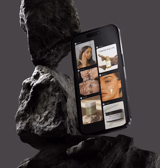 A smartphone leaning against stacked rocks, showing a Mary Louise product gallery with skincare images and product ads on the screen.