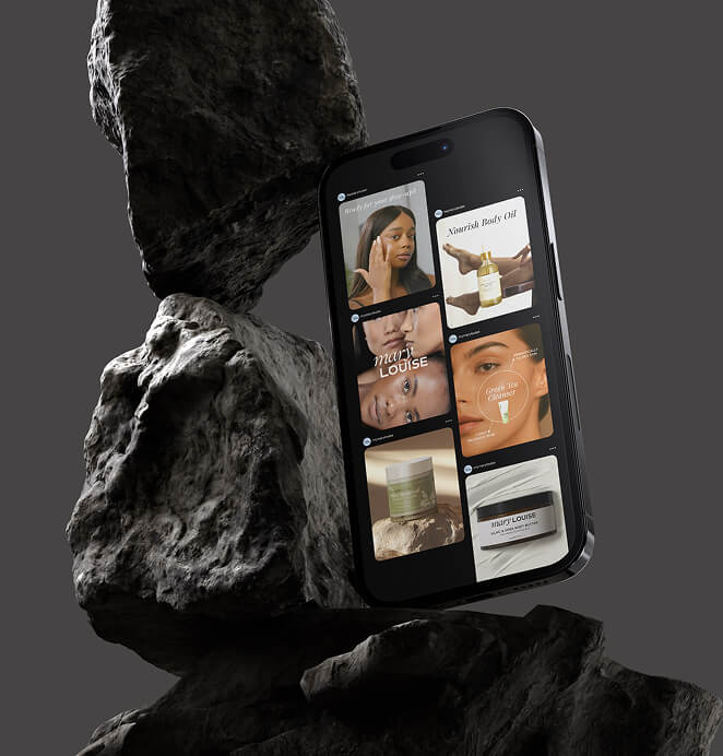A smartphone leaning against stacked rocks, showing a Mary Louise product gallery with skincare images and product ads on the screen.