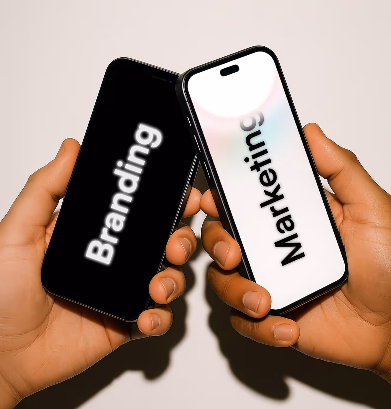 Two hands each holding a smartphone, positioned to face each other. The black phone on the left displays the word “Branding” in white text, while the white phone on the right shows the word “Marketing” in black text. The image symbolizes the connection between branding and marketing.