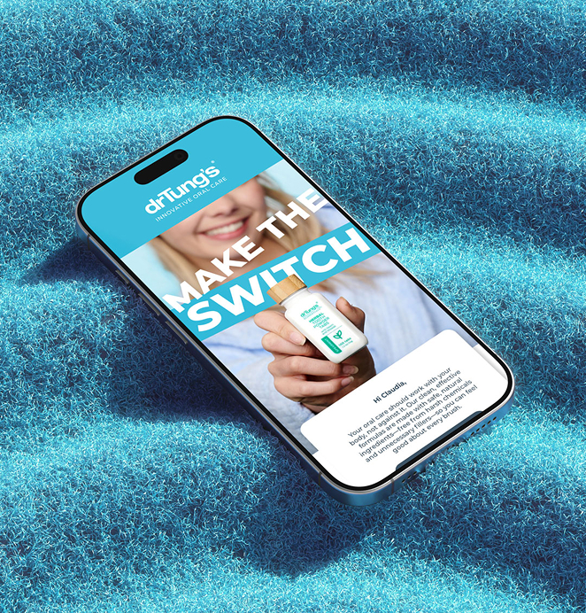 A smartphone lying on bright blue textured fabric, displaying a drTung’s Innovative Oral Care ad with the slogan 'Make the Switch' and an image of a woman holding the product.