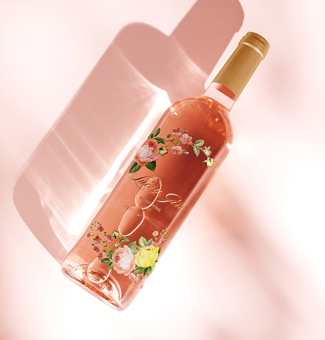 A bottle of Lucky Girl rosé wine with floral illustrations on the label, photographed against a soft pink background with light reflections.