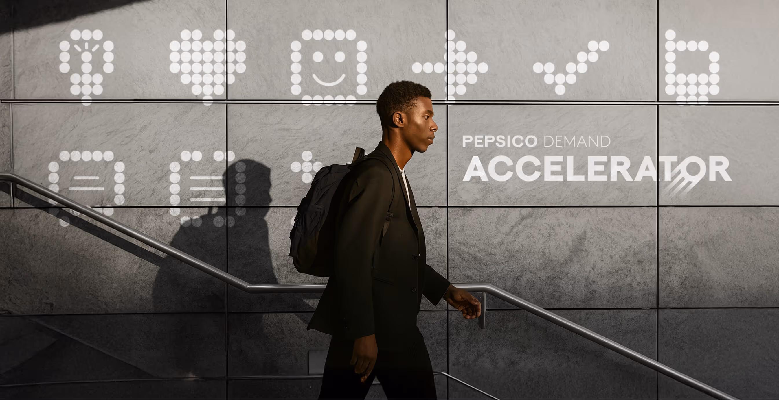 Man with backpack walks up stairs past a wall displaying illuminated dot icons and the text “PepsiCo Demand Accelerator.” The design conveys innovation and data-driven branding.
