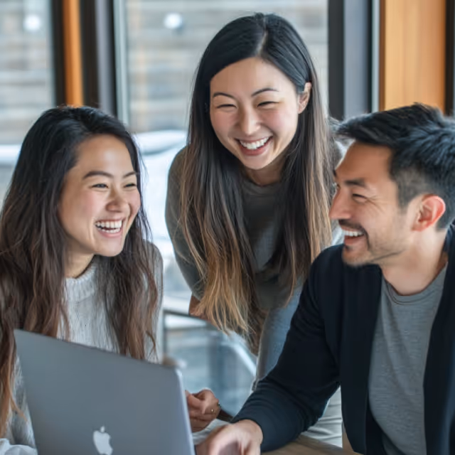 Three colleagues smiling and collaborating over a laptop. They appear excited, representing teamwork, brainstorming, and positive workplace culture.