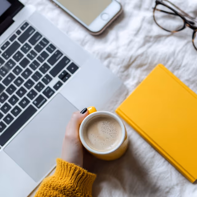 A flat lay of a creative workspace with colorful paper sheets, a laptop, pens, and a cup of coffee, arranged neatly.