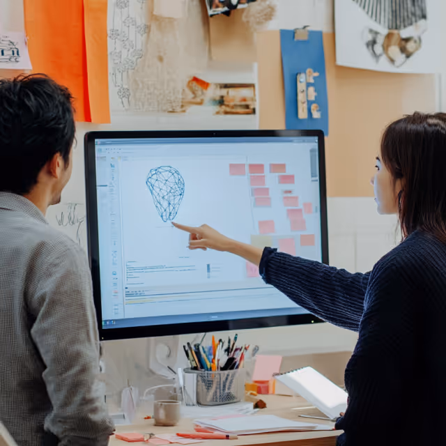 Two designers working together on a digital sketch of a gemstone on a large monitor, surrounded by creative materials and inspiration boards.