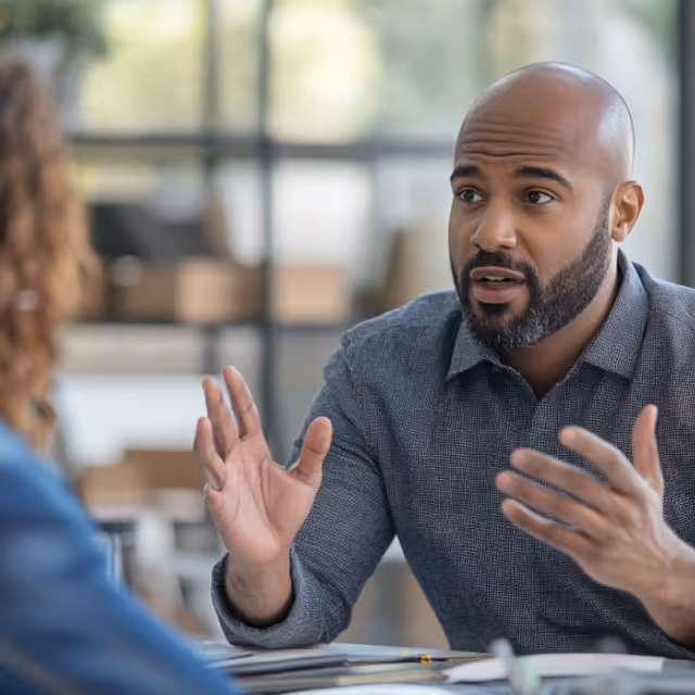 A man gesturing expressively while speaking during a business meeting, emphasizing communication and strategic discussion.