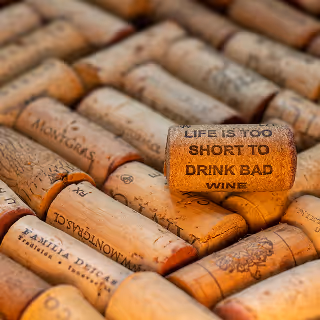 A collection of natural wine corks arranged closely together, with one cork prominently reading “Life is too short to drink bad wine.”