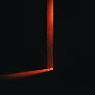 A solitary silhouette stands in a towering vertical doorway with dramatic red light spilling into a dark surrounding, evoking mystery, potential, and discovery.