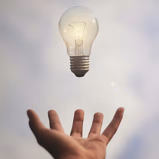 A glowing light bulb floating above an outstretched hand against a cloudy sky, symbolizing innovation and creative ideas.