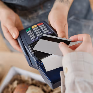 A close-up of a credit card being tapped on a point-of-sale terminal during a purchase, representing a transaction or payment process.
