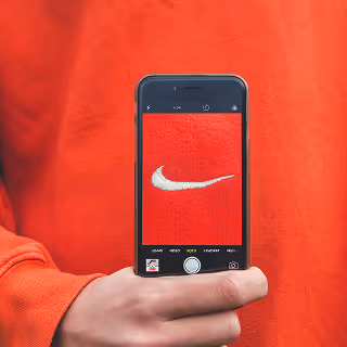 Hand holding a phone displaying a photo of a Nike logo against a red shirt, representing strong brand identity.