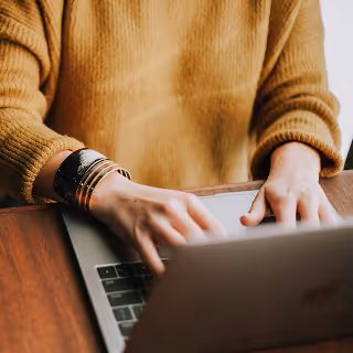 Close-up of a person in a mustard sweater typing on a laptop, suggesting focus and productivity.