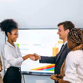 Two professionals shake hands in front of a screen showing a colorful bar chart, while colleagues stand nearby smiling.