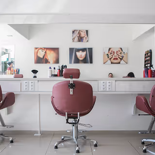 A clean and modern salon space with pink styling chairs, white countertops, and posters of hairstyles above a large mirror.