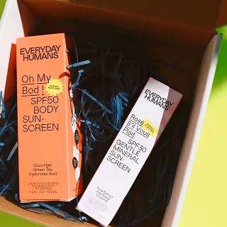 Open cardboard box with shredded navy blue paper inside, containing two vibrant sunscreen product boxes labeled "EVERYDAY HUMANS."