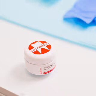 Small white dental product container labeled “Septodont” placed on a blue mat with latex gloves nearby.