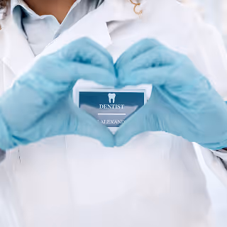 Dentist in a lab coat and blue gloves forms a heart shape with hands over a name badge labeled “Dentist.”