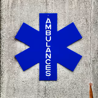 A bold blue asterisk sign labeled “Ambulances” on a concrete wall, indicating emergency medical service access.