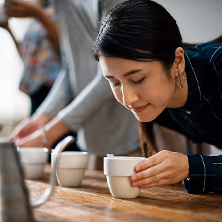 A woman thoughtfully smells a cup during a structured aroma-testing session, conveying an atmosphere of careful sensory exploration and professional evaluation.