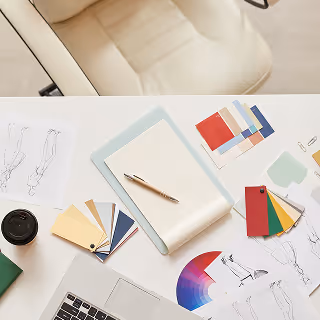 A workspace setup showing a neat desk with sketches, colorful swatches, color wheels, and an open notepad, capturing the early stages of creative logo and brand identity design.