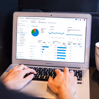 Close-up of hands typing on a laptop displaying detailed digital analytics, charts, and data visualizations, highlighting the analytical aspect of digital branding.