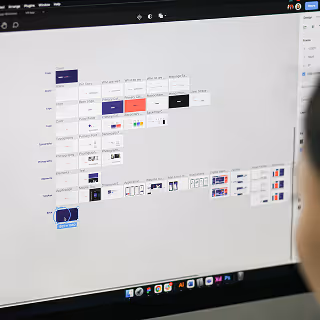 Designer viewing a digital workspace on a monitor displaying organized wireframes and UI layouts, showcasing meticulous digital design planning.